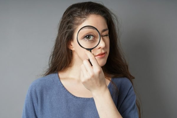 A young woman looking through magnifying glass. Symbol for spy audit or search concept.