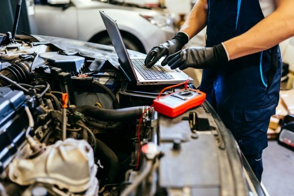 Car mechanic at work. Car an electrician using computer in auto repair shop. Close up.